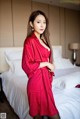 A woman in a red robe standing on a bed.