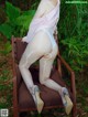 A woman in a white bodysuit sitting on a brown chair.