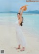 A woman in a white dress holding a straw hat on the beach.