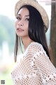 A woman wearing a straw hat leaning against a tree.