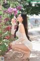 A woman in a white dress sitting on a sidewalk next to flowers.