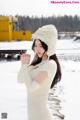 A woman in a white sweater and a fur hat in the snow.