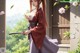 A woman in traditional attire holds a sword, standing near a window with cherry blossoms.