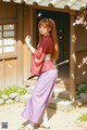 A woman in traditional attire stands near a wooden structure with cherry blossoms.