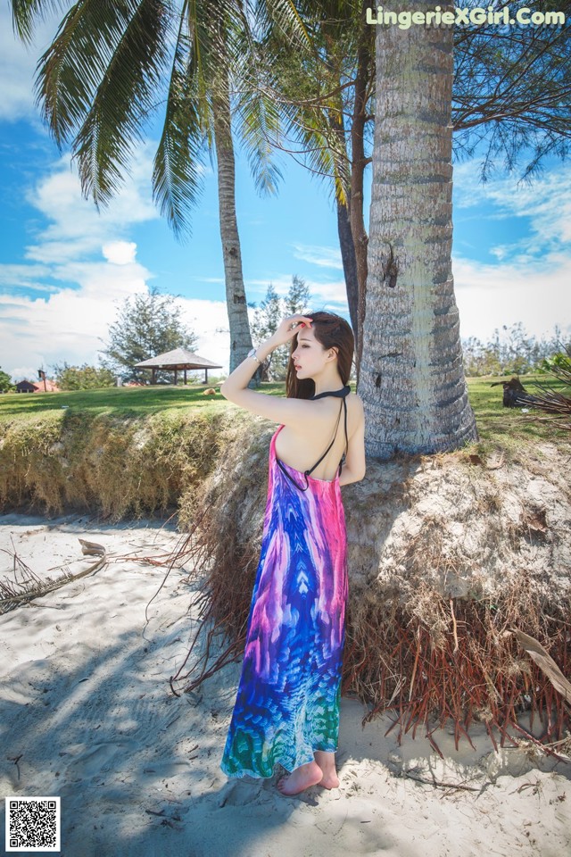A woman in a colorful dress standing next to a palm tree.