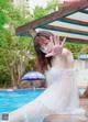 A woman in a white dress sitting by a swimming pool.