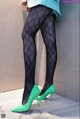 A woman wearing black tights and green high heels.