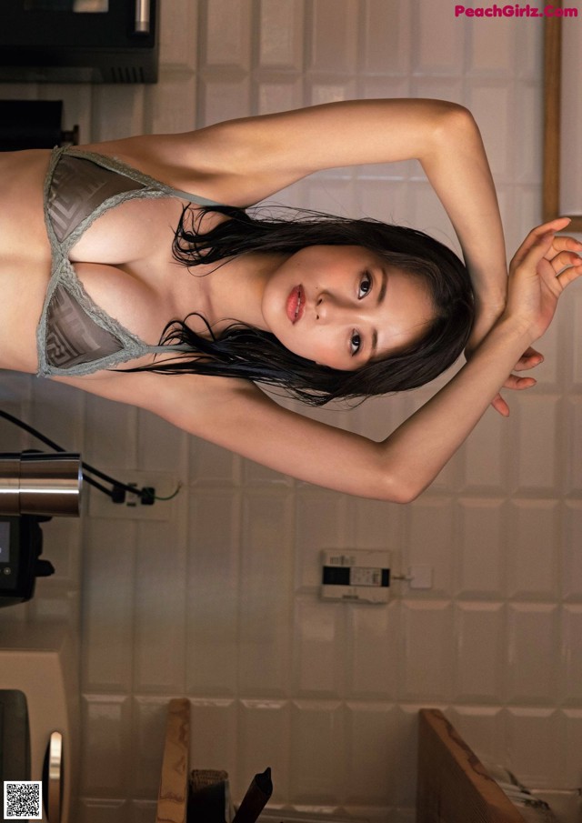 A woman in a gray lingerie posing in a kitchen.