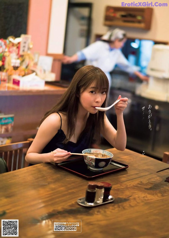 A woman sitting at a table eating a bowl of food.