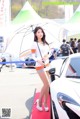 A woman holding an umbrella standing next to a white car.