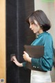 A woman in a green shirt and white skirt holding a brown folder.