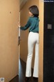 A woman in a green shirt and white pants standing in front of a door.