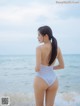 A woman in a white swimsuit standing on the beach.