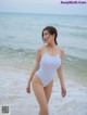 A woman in a white swimsuit standing on the beach.